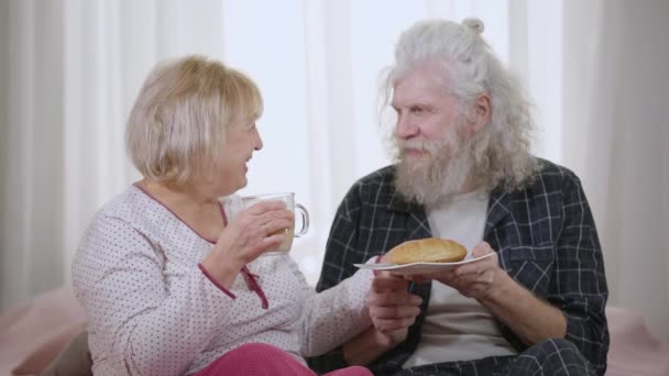 大老婆慢吞吞地把羊角面包和咖啡杯递给心爱的丈夫 早上在家照顾男人的可爱的白人女人笑着 关系和休闲概念 — 图库视频影像
