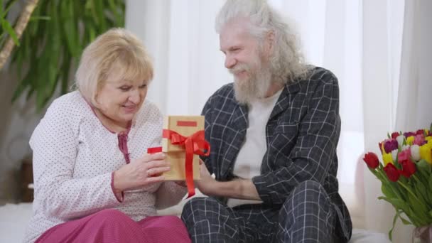 Uśmiechnięty Starszy Mąż Rozmawiający Podekscytowaną Żoną Badającą Prezent Siedzącą Domu — Wideo stockowe