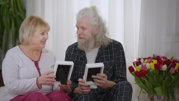 Smiling Senior Couple Pajamas Recalling Memories Watching Old Photos Talking — Vídeo de stock
