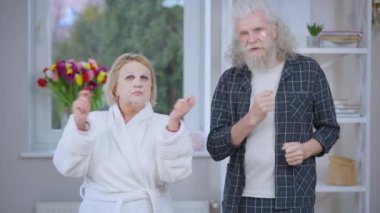 Neşeli yaşlı çift sabahları kameraya bakıp maske ve göz bandı takıyor. Olumlu neşe saçan Kafkasyalı karı koca hafta sonu evde keyif çatıyor.