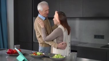 Loving senior Caucasian couple dancing in kitchen in the morning talking. Smiling relaxed husband and wife enjoying leisure together at home indoors. Eternal love and lifestyle concept