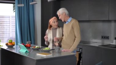 Positive smiling couple of senior bloggers talking cooking in kitchen at home. Happy confident Caucasian man and woman enjoying vlogging indoors smiling