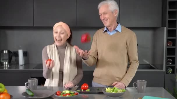 在厨房的柜台前 一对中年夫妇欢快地跳着红番茄和胡椒粉 一边笑着 无忧无虑的 快乐的白人夫妻 在家里尽情地烹调健康的沙拉 — 图库视频影像