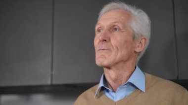 Close-up portrait of handsome senior Caucasian man drinking coffee looking away in kitchen at home. Happy relaxed male retiree enjoying morning thinking standing on the right