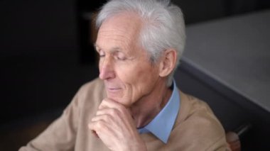 High angle view portrait of sad senior Caucasian man praying sitting at home looking away. Depressed lonely male retiree in wheelchair thinking indoors. Hope and health care concept