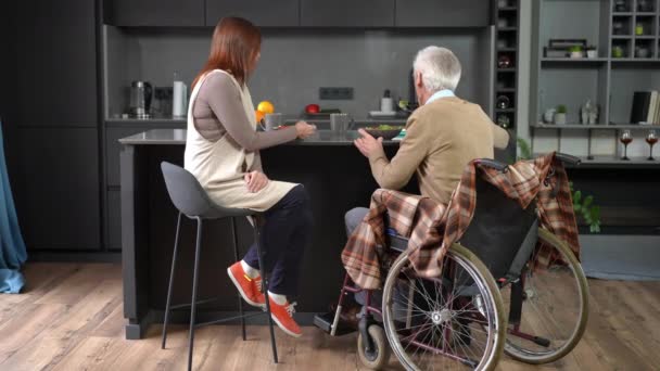 Orolig Äldre Kvinna Som Äter Hemma Med Irriterad Man Rullstol — Stockvideo