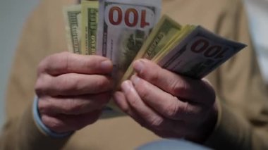 Close-up male senior hands counting cash money indoors. Front view unrecognizable Caucasian old man calculating income planning expenses at home