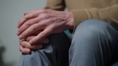Close-up senior male hand rubbing ill knee indoors. Unrecognizable Caucasian man stroking leg sitting at home. Health care and aging concept