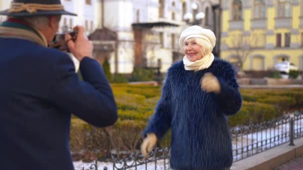 为男人在城市街道上拍照而摆出一副快乐而积极的老年女子的样子 在欧洲与丈夫一起享受退休旅行的美满幸福的白人优雅妻子 — 图库视频影像