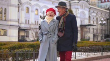 Hugging loving couple of senior tourists walking on city street talking. Smiling happy Caucasian husband and wife travelling in Europe outdoors strolling enjoying trip