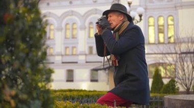 Side view talented male senior photographer taking photo on city street in Europe. Confident handsome elegant Caucasian man photographing with camera outdoors travelling. Tourism and talent