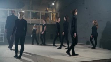 Panning shot of backstage with young actors and actresses strolling with serious facial expressions. Confident talented Caucasian men and women in black rehearsing performance in theatre