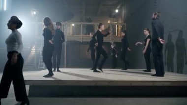 Wide shot talented men and women rehearsing theater performance on backstage doing lunges looking up at raised hand. Skilled Caucasian actors and actresses playing with director walking gesturing