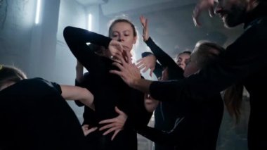 Theatrical troupe moving hands around body of young slim actress at backlit. Young talented Caucasian men and women rehearsing modern play on backstage indoors. Performance and art concept