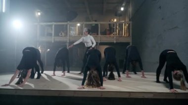 Wide shot concentrated theater director leading rehearsal as young actors and actresses walking with hands to plank position. Skilled Caucasian men and women rehearsing on backstage