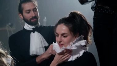 Portrait of smiling young Caucasian actress on backstage with actor helping putting on neck ruff. Positive talented confident woman and man getting ready for show in theater. Performance and art