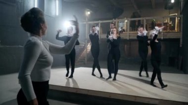 Group of young talented men and women in black with white neck and wrist ruff rehearsing performance repeating after stage director and leading actress. Concentrated artists getting ready on backstage