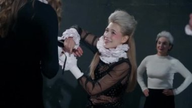 Young woman smiling talking with colleagues putting on stage costumes on backstage. Beautiful talented Caucasian actress helping actors getting ready for theater show