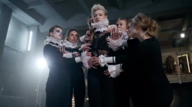 Zoom in portrait of gorgeous Caucasian young actress looking at camera as troupe stretching hands to leading character. Confident serious woman posing rehearsing role on backstage