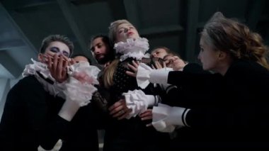 Professional talented actresses and actors stretching hands admiring leading character and looking at camera. Young Caucasian men and women in retro costumes posing on backstage bottom angle view