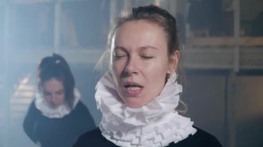 Close-up skilled actress rehearsing stretching facial muscles looking at camera getting ready for show. Portrait of Caucasian young concentrated woman posing on backstage in theater