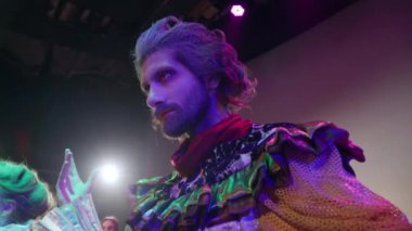 Panning around handsome professional actor in vintage costume acting on stage in spotlight. Concentrated Caucasian bearded man with serious facial expression looking away playing role in show
