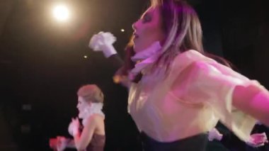 Carefree woman jumping dancing on stage with actors moving at background. Skilled Caucasian young actress performing in theater play. Acting and art concept