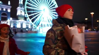 Loving confident teen boy looking away as girl surprising boyfriend tapping shoulder. Happy Caucasian couple dating on night city street on Valentines. Slow motion