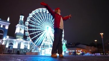 Wide shot excited teen girl spinning on night street with bouquet of flowers. Bottom angle view of happy confident Caucasian teenager with Valentines girl rejoicing outdoors. Slow motion