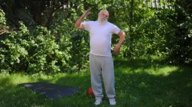 Wide shot senior Caucasian bearded man warming up training outdoors looking at camera. Portrait of motivated positive retiree working out on backyard on sunny summer day posing. Sport and aging