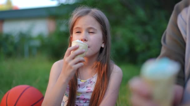 公園の夕日に座っているおいしいアイスクリームを楽しむリラックスした幸せな女の子の肖像画 祖父と屋外でピクニックに白人の孫娘 スローモーション — ストック動画