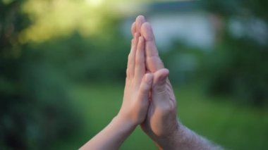 Close-up side view little female hand and senior male palm together outdoors. Unrecognizable Caucasian granddaughter and grandfather in summer park at sunset. Bonding and family concept