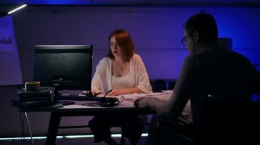 Beautiful concentrated woman analyzing e-market surfing Internet on PC as man in wheelchair analyzing paperwork. Young Caucasian startupers thinking planning business idea in garage indoors