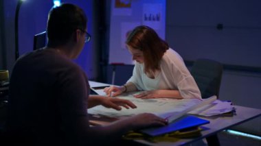 Rack focus from concentrated positive young woman talking examining architectural blueprint to focused man discussing idea with colleague. Creative Caucasian coworkers planning project in garage