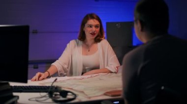 Portrait of smiling redhead woman talking with man sitting at table with paperwork. Positive confident intelligent Caucasian freelancer discussing business project with startuper in garage