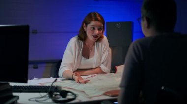 Positive curious young redhead Caucasian woman talking with man sitting at table with paperwork making surprised facial expression. Portrait of beautiful startuper discussing idea with freelancer