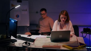 Young intelligent architect sitting at table planning idea as colleague in wheelchair entering garage greeting. Smiling confident Caucasian man and woman talking analyzing project indoors