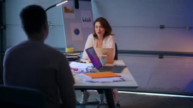 Portrait of confident young startuper meeting with partner in garage talking sitting at table. Intelligent Caucasian woman discussing cooperation with unrecognizable man planning business