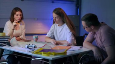 Team of creative architects discussing project analyzing blueprint sitting in garage indoors. Concentrated smart young Caucasian man and women talking planning startup idea. Intelligence and business