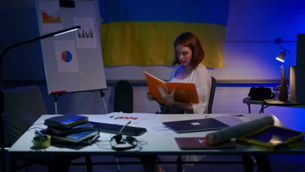 若い陽気なフリーランスは ガレージの計画のスタートアップに座って椅子に回転 背景にウクライナのフラグで書類を分析幸せな自信の美しい女性の肖像画 — ストック動画