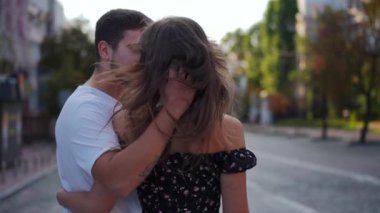 Panning around young handsome man kissing gorgeous slim woman standing on city street talking and smiling. Happy loving Caucasian boyfriend and girlfriend dating enjoying summer spring leisure