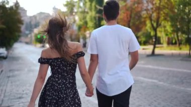 Gorgeous young slim woman turning looking at camera walking with man on city street in slow motion. portrait of confident charming Caucasian girlfriend posing strolling with boyfriend outdoors