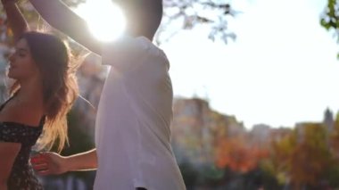 Happy young Caucasian man spinning woman standing in sunbeam on city street. Loving millennial boyfriend dating with girlfriend at sunset outdoors dancing in slow motion