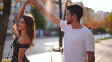 Side view smiling loving man admiring woman spinning in slow motion in sunshine on city street. Happy millennial Caucasian handsome boyfriend enjoying dating with cheerful girlfriend outdoors
