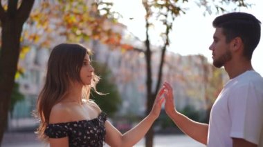 Side view beautiful woman and handsome man standing on city street putting hands together looking at each other. Medium shot portrait of confident Caucasian millennial couple in sunshine outdoors