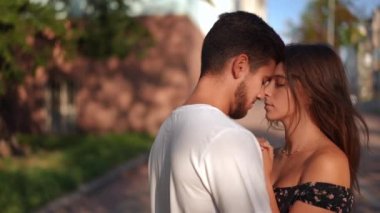 Zoom in to loving young couple with closed eyes rubbing noses in slow motion standing on the right outdoors. Happy relaxed confident Caucasian man and woman enjoying dating in city
