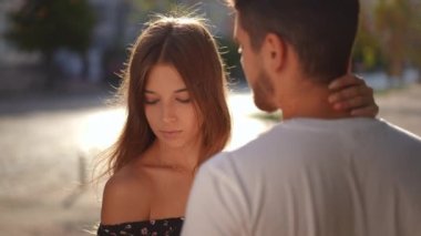 Young man caressing shoulder and neck of beautiful slim woman turning partner face. Happy tender Caucasian boyfriend stroking girlfriend standing on sunny city street. Love and bonding concept