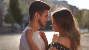 Side view close-up laughing loving young couple hugging standing in sunrays on city street. Happy confident carefree Caucasian boyfriend and girlfriend in sunshine outdoors. Dating and love concept