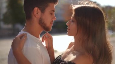 Side view smiling loving young woman touching face of handsome bearded man standing in sunshine on city street. Happy confident Caucasian millennial girlfriend dating with boyfriend at sunrise