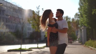 Medium shot of smiling loving young boyfriend spinning girlfriend in slow motion on city street. Happy satisfied Caucasian woman raising legs hugging man laughing. Bonding and love concept